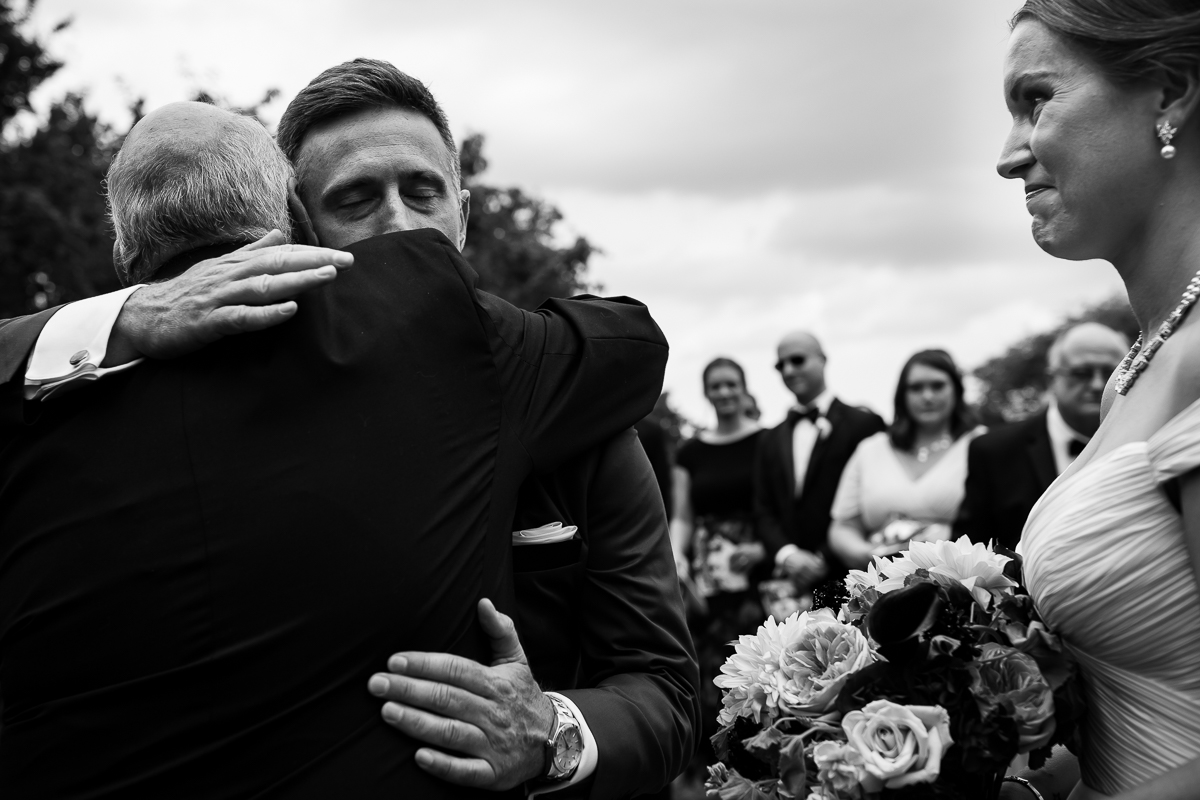 emotional heartfelt wedding photographer father of bride hugs groom while giving away bride at altar