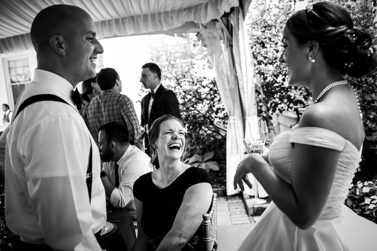 river farm wedding reception best emotional candid wedding photographer black and white photo of bride talking and laughing with guests during cocktail hour under tent