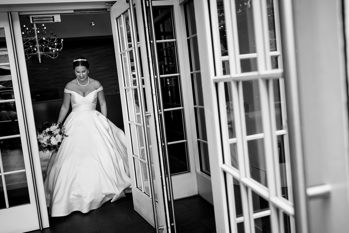 black and white photo of bride leaving Kimpton Lorien hotel during first look wearing ballgown with off the shoulder sleeves