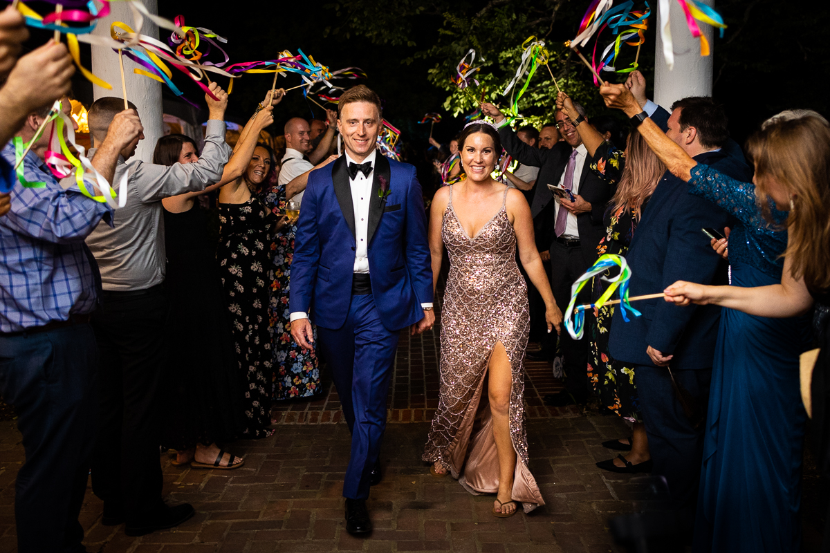 best award winning authentic colorful vibrant wedding photographer bride and groom make final exit during reception with guests waving colorful streamers