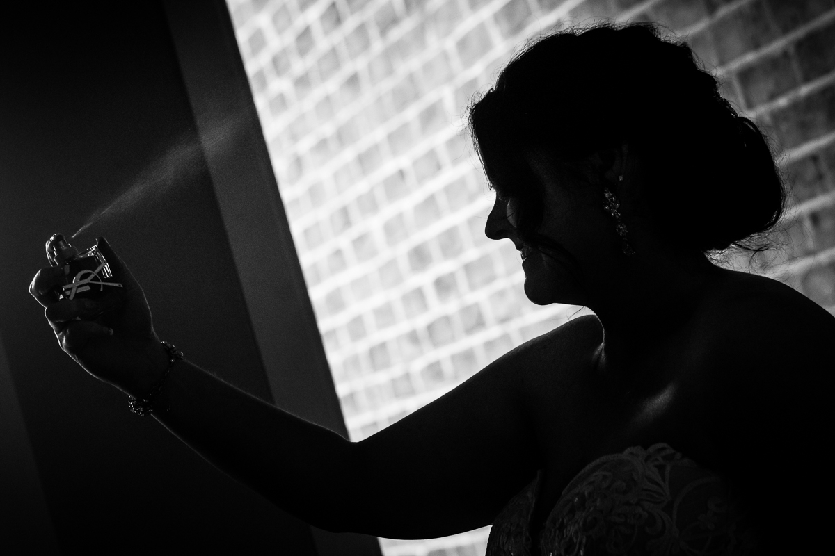 unique fun creative black and white photo of bride spraying perfume on wedding day with brick wall behind gettysburg