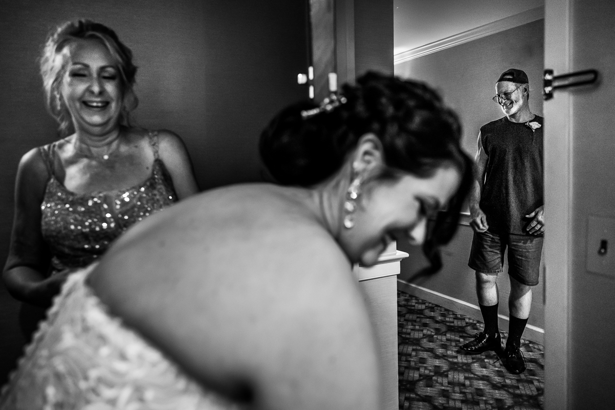 authentic candid wedding photographer bride getting ready in hotel room while mom helps her all laughing and smiling