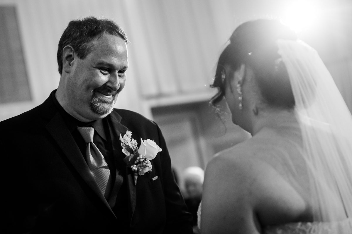 emotional authentic black and white photo of groom smiling at bride as she stands in front of him during ceremony 