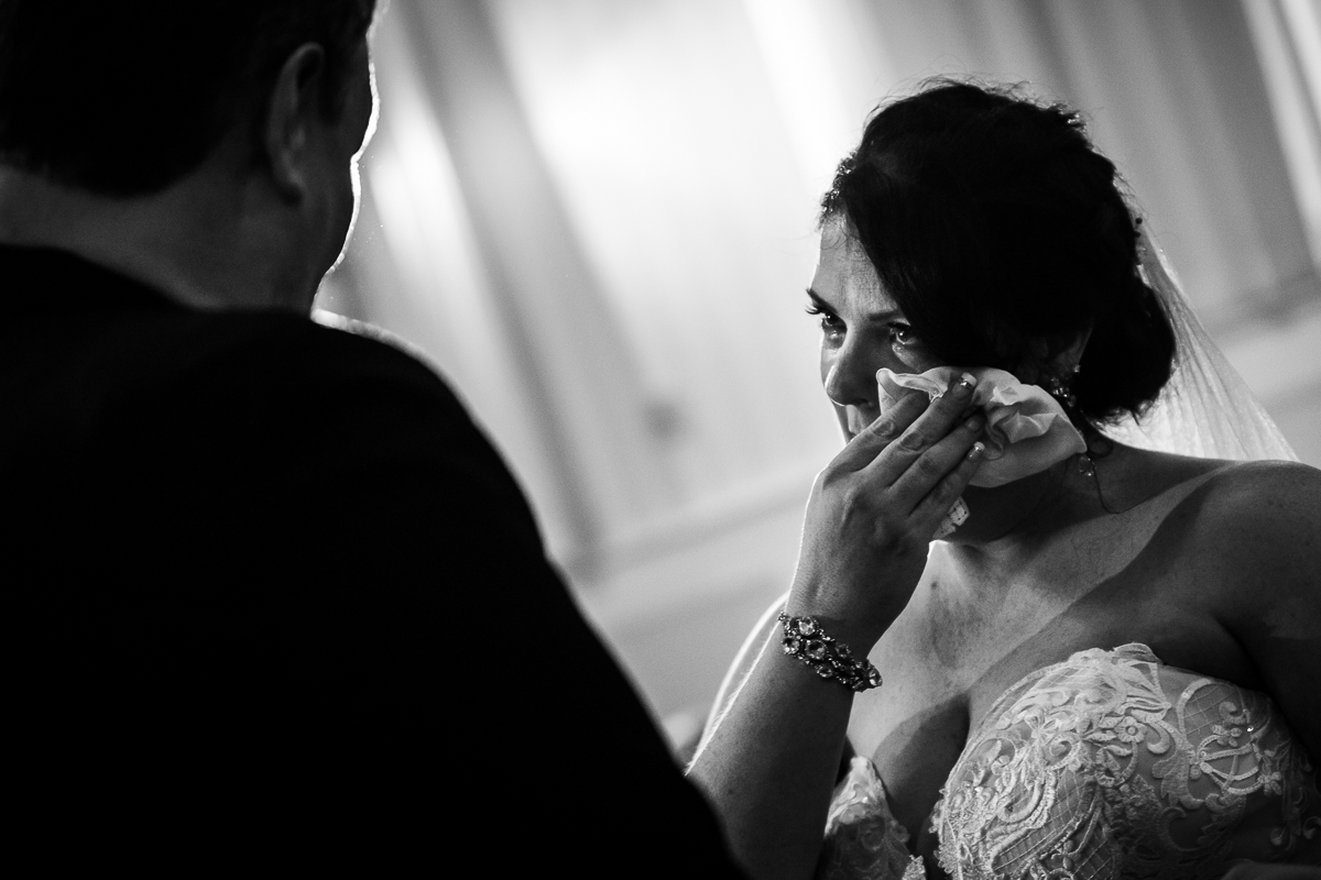 black and white photo of bride crying during wedding ceremony wiping tear away with tissue emotional award winning wedding photographer