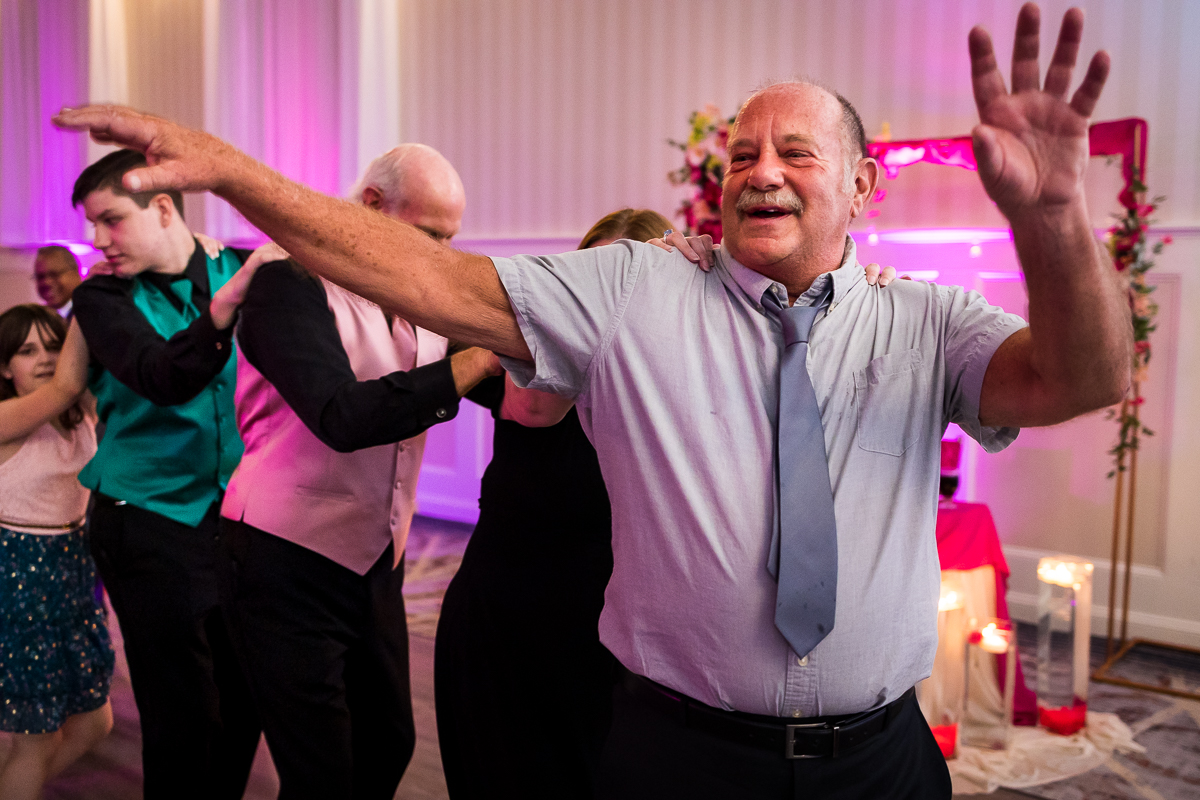 man laughs and dances during wedding reception start of conga line