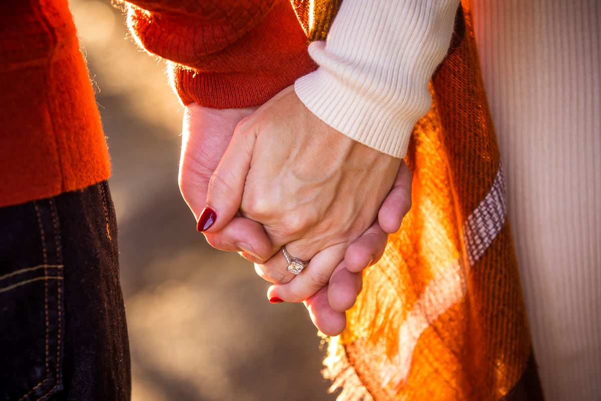close up of couple holding hands wearing radiant engagement ring fall colors