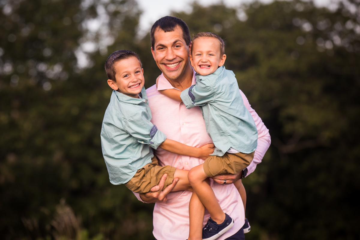 joyful family photographer Lehigh valley central pa dad holding both sons in each arm smiling outside traditional family portrait 