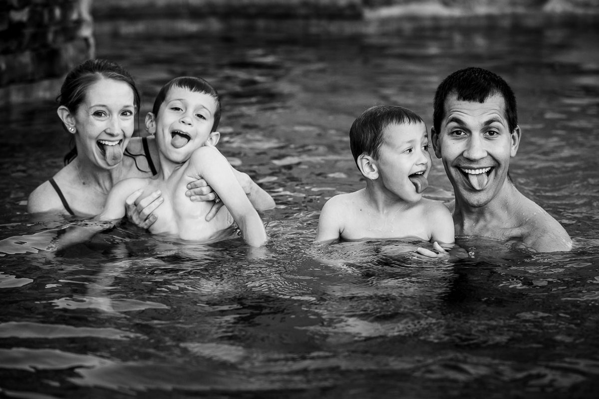 black and white photo of family sticking tongues out in swimming pool 