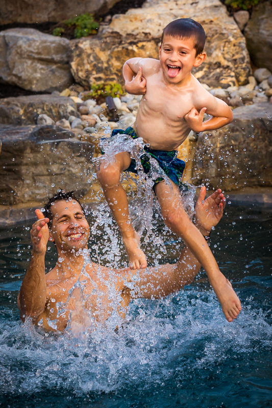 dad throwing son in swimming pool both laughing and smiling