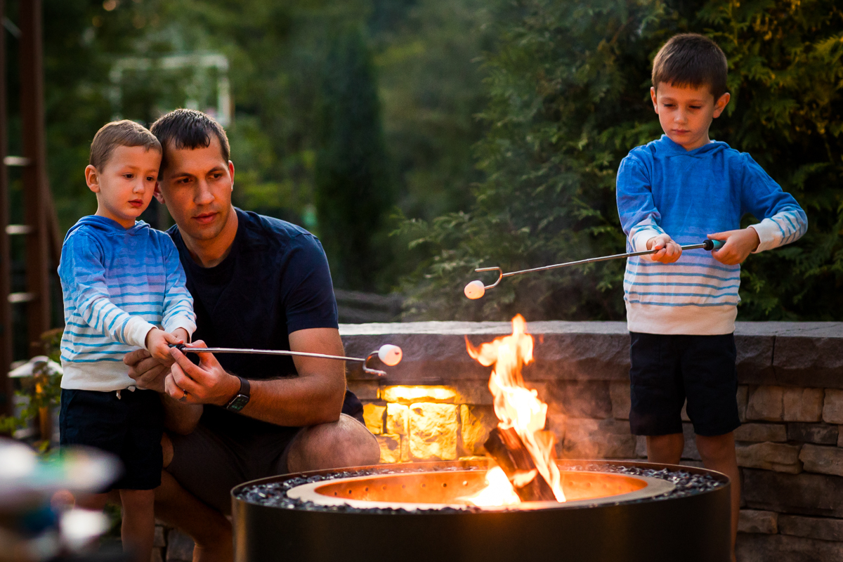 dad and sons sitting in front of fire pit roasting marshmallows at home central pa lifestyle family photographer