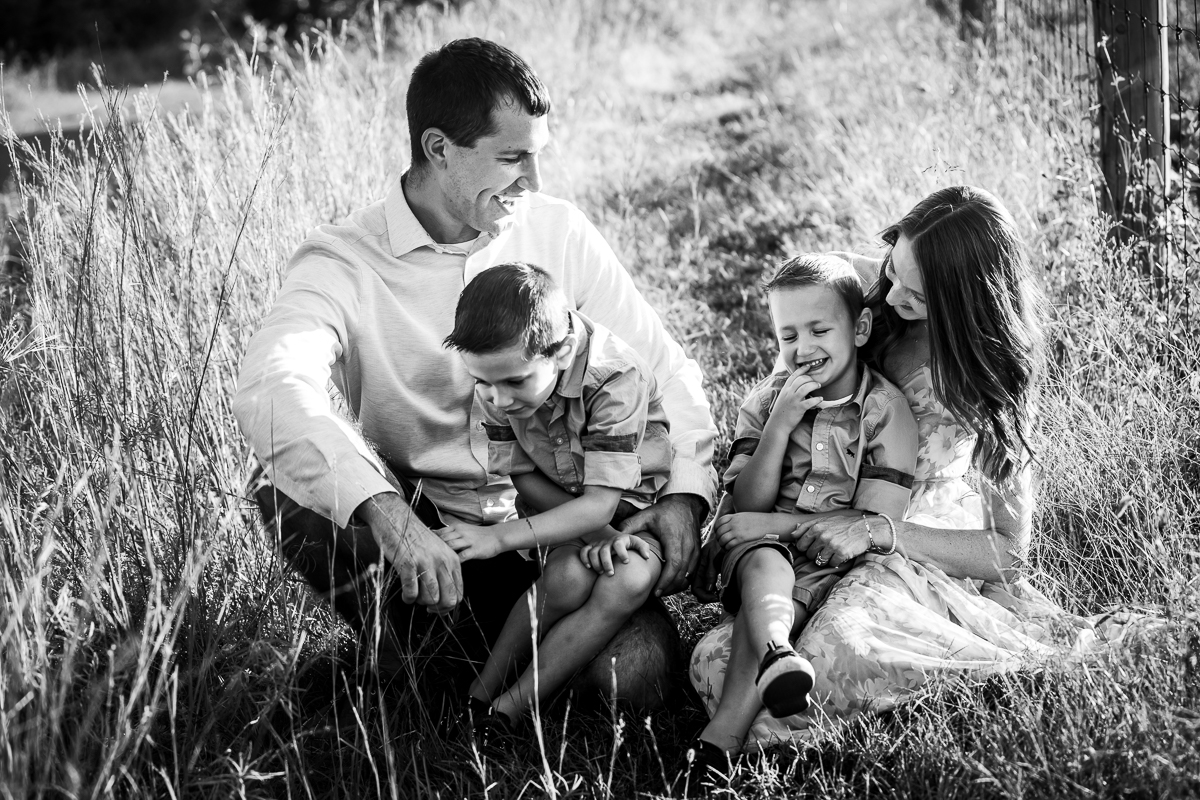 black and white photo lifestyle family photographer family sitting in grass Lehigh valley laughing and smiling