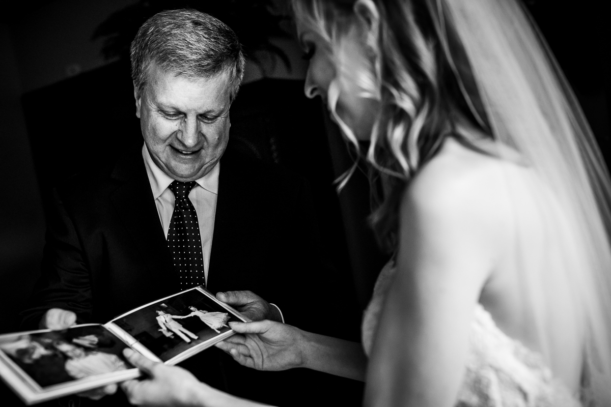 black and white photo of bride and father smiling while looking at photo album 