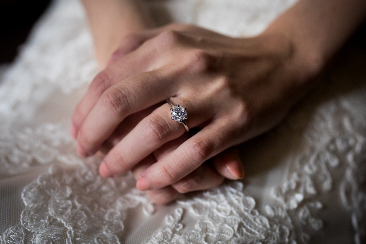 close up detail photo of bride's hands wearing round diamond ring with gold band