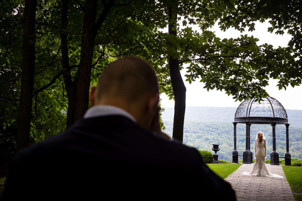authentic candid vibrant wedding photographer groom standing with eyes closed while bride walks toward him during first look with amazing views at stroudsmoor ridgecrest ceremony site