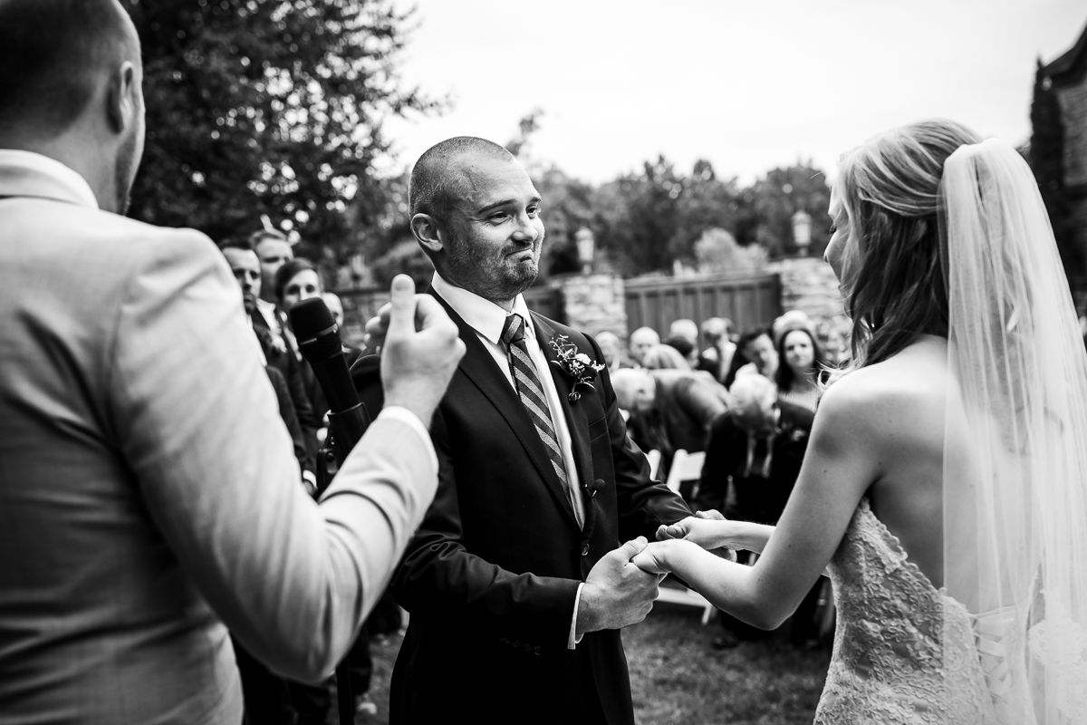 authentic emotional candid black and white photo Stroudsmoor Terraview wedding ceremony bride and groom hold hands while groom smiles at bride during vows