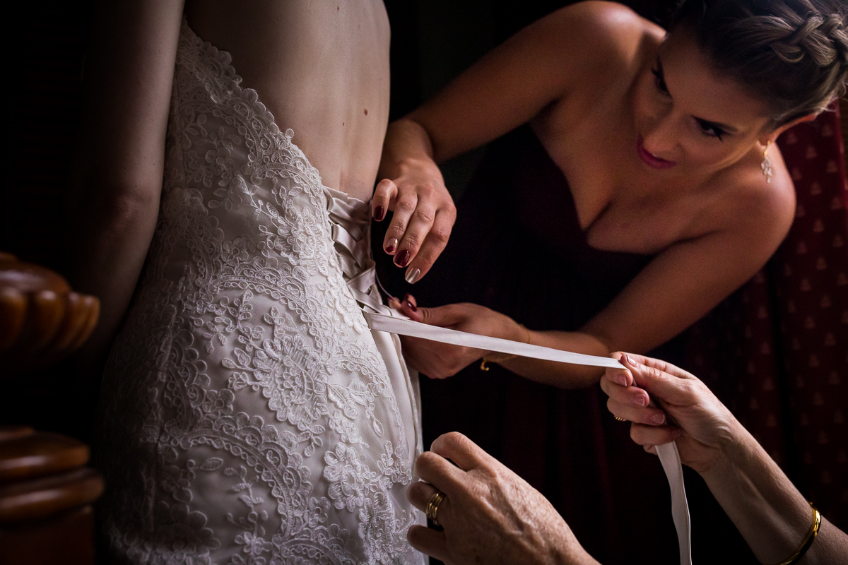 bridesmaids lacing up corset back of bride's lace wedding dress in ledgemere suites
