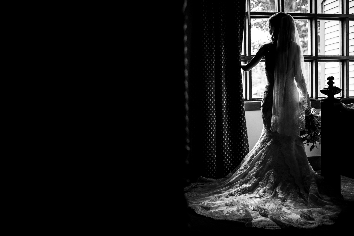 stroudsmoor country inn ledgemere suites black and white photo of bride standing in front of window looking outside holding bouquet