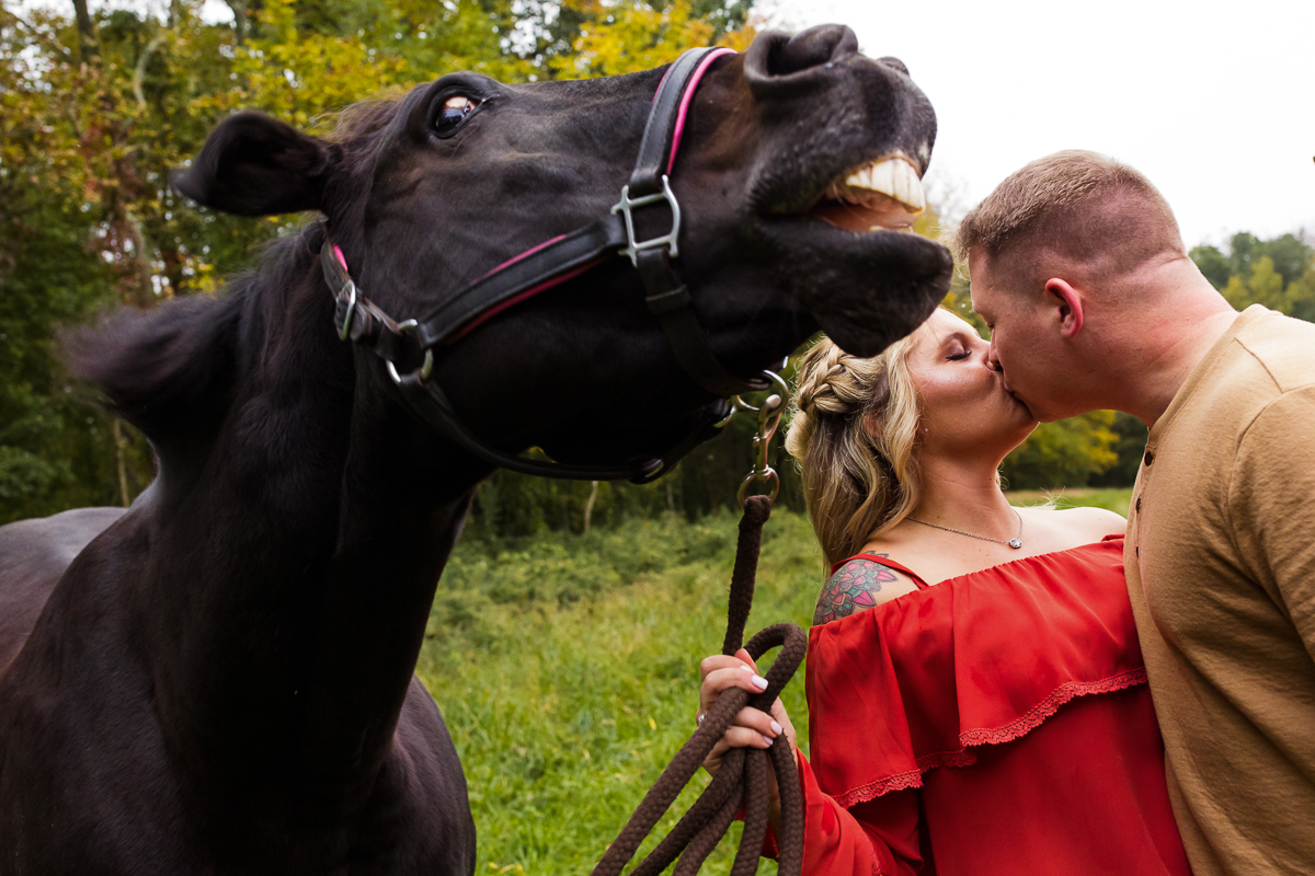 creative artistic engagement photographer horse smiling with couple kissing behind it at Blairstown nj barn