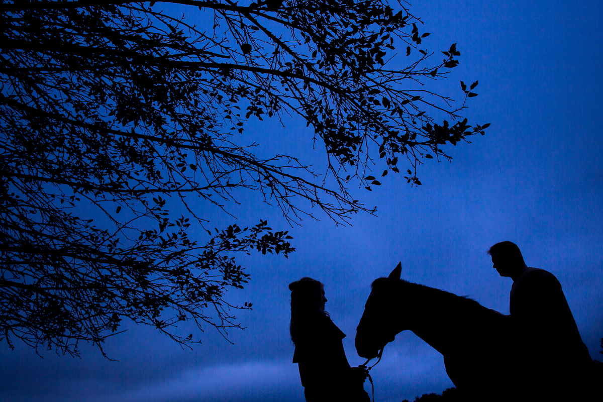 horseback riding and fly fishing engagement best engagement photographer couple with horse silhouetted against blue sky