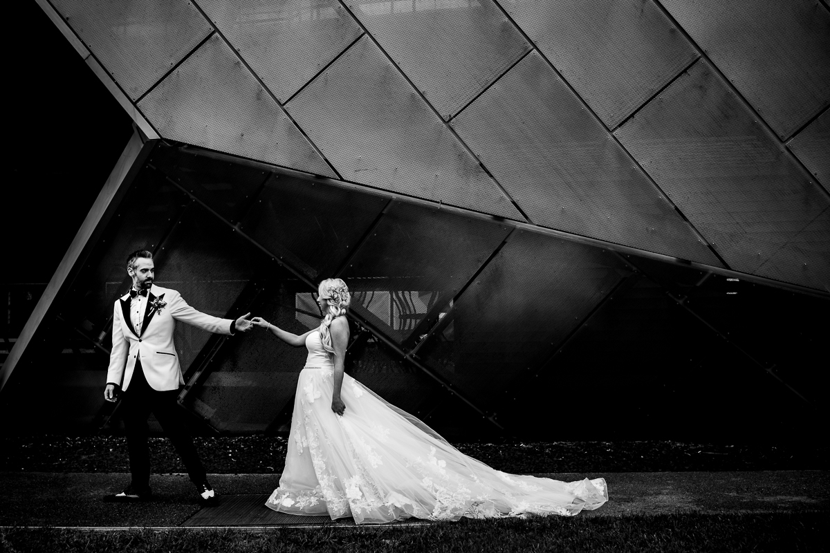 black and white photo of groom leading bride by the hand in front of unique architecture at arts quest steel stacks Bethlehem pa