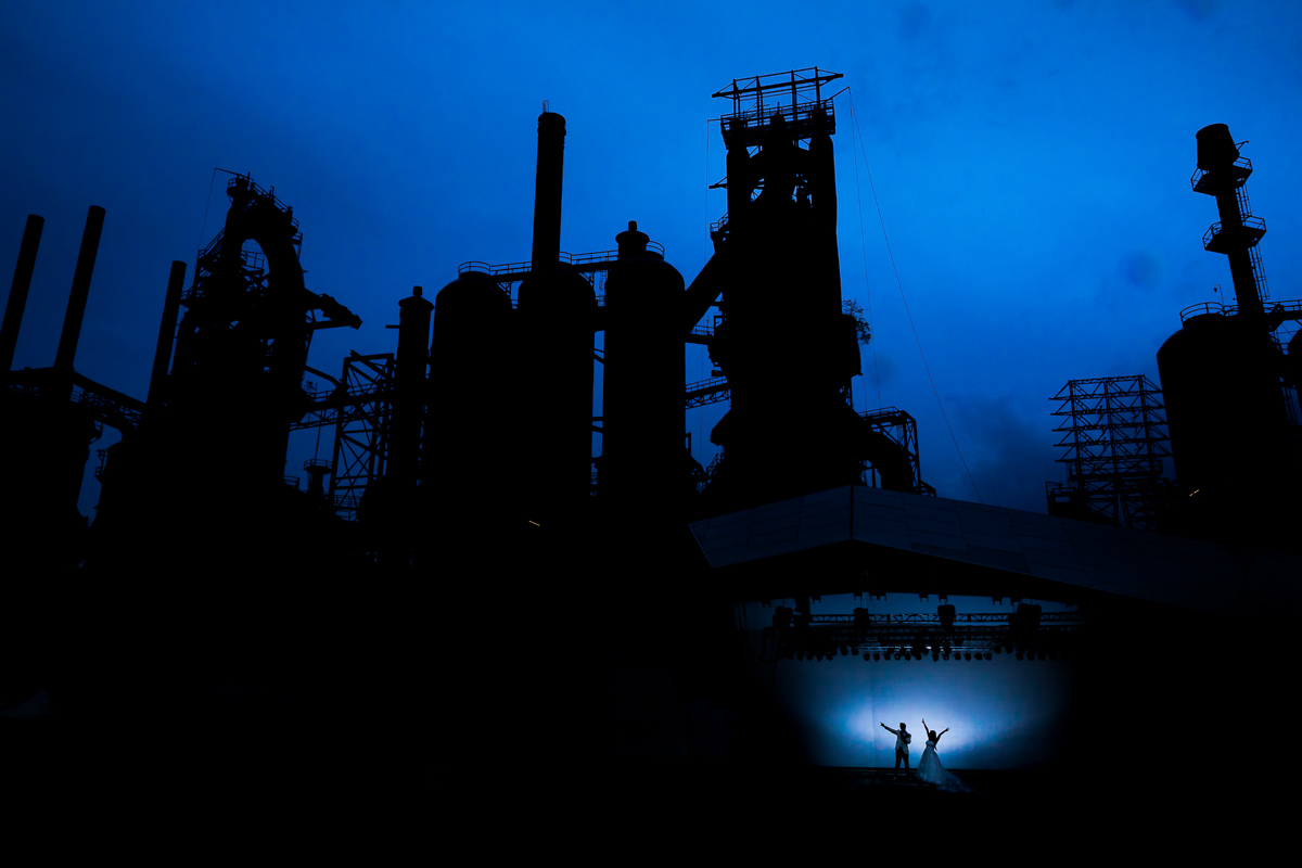 best award winning unique artistic creative wedding after-session photographer steelstacks silhouetted against vibrant blue sky bride and groom stand at the bottom with hands up