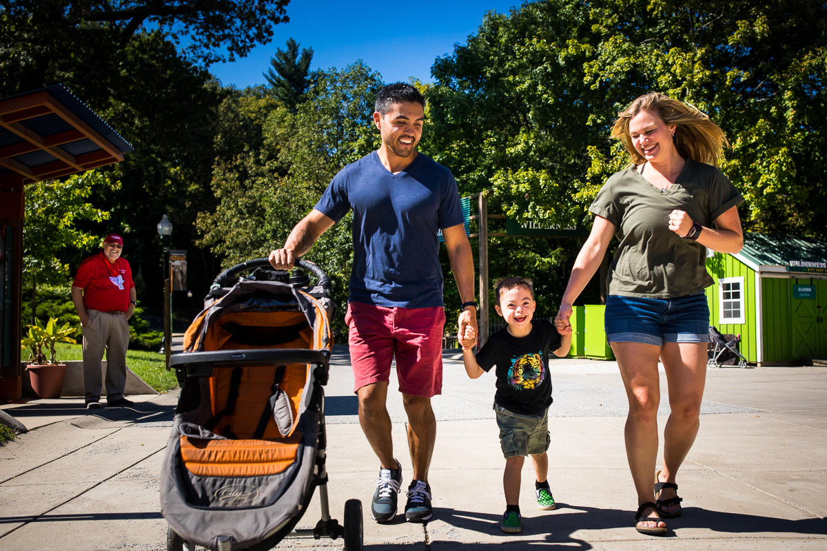 parents walking with son pushing stroller at Maryland zoo smiling and laughing fun joyful family lifestyle photographer