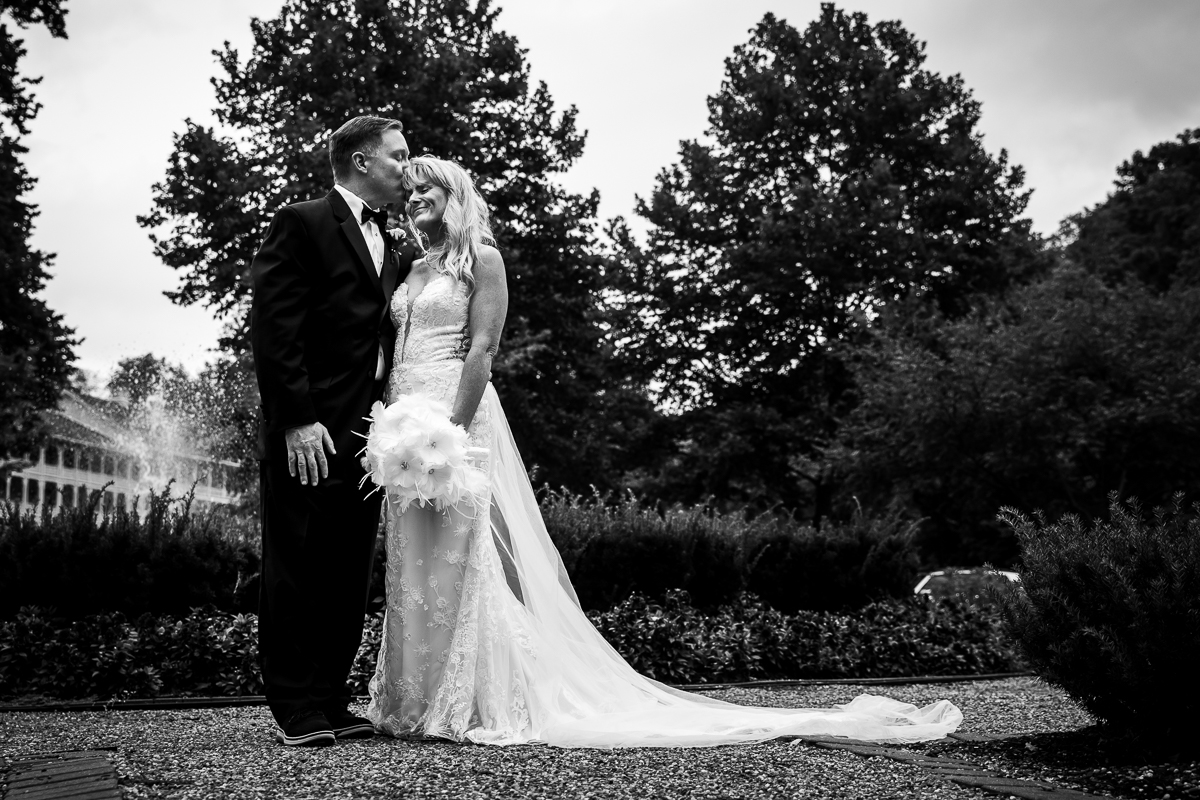 Omni Bedford Springs wedding photographer black and white photo of groom kissing bride on top of head with omni in the background