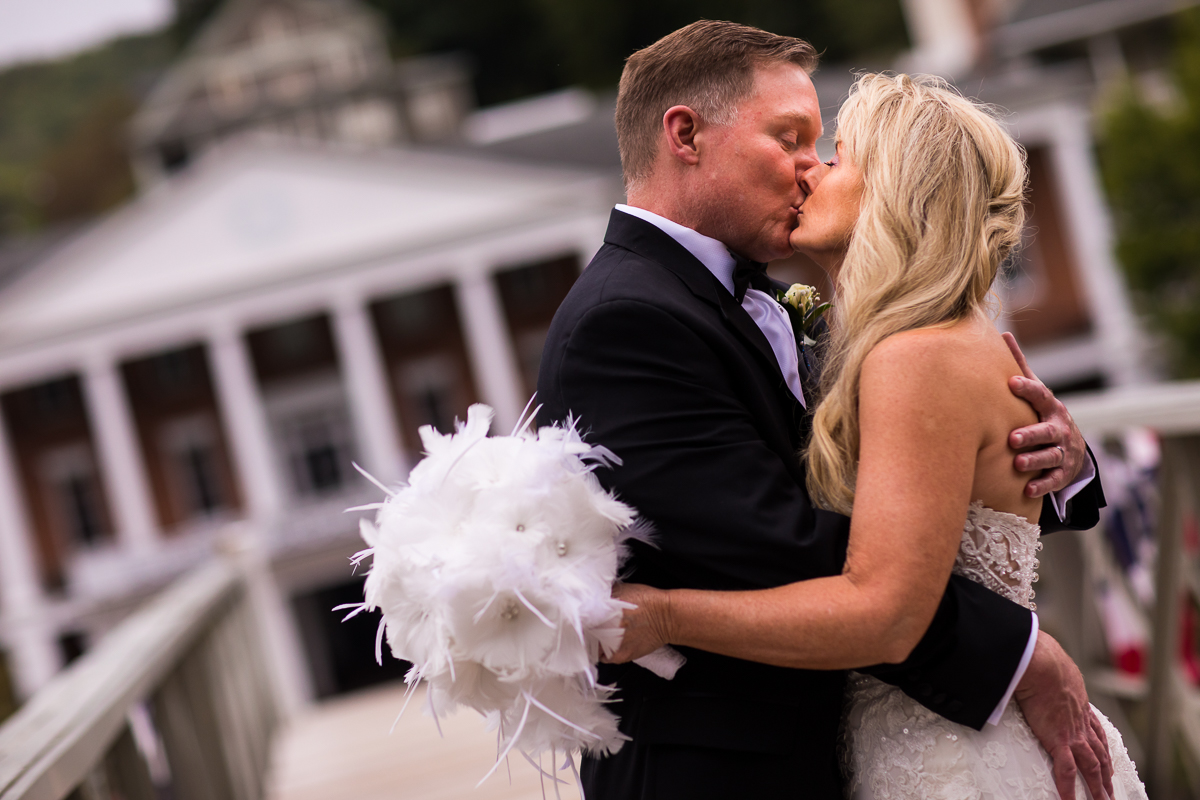 Omni Bedford Springs wedding photographer bride holding white feather bouquet and groom share a kiss with omni in the background