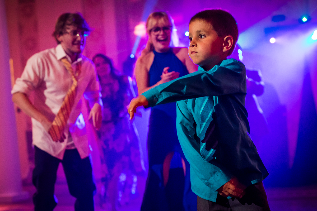 little boy dancing at wedding reception while guests cheer and smile at him
