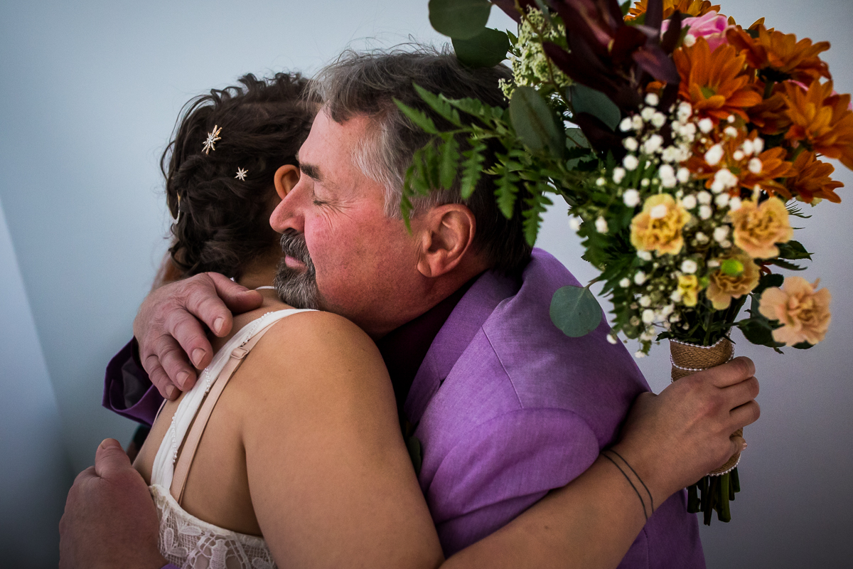 bride hugging dad holding flower bouquet before wedding ceremony