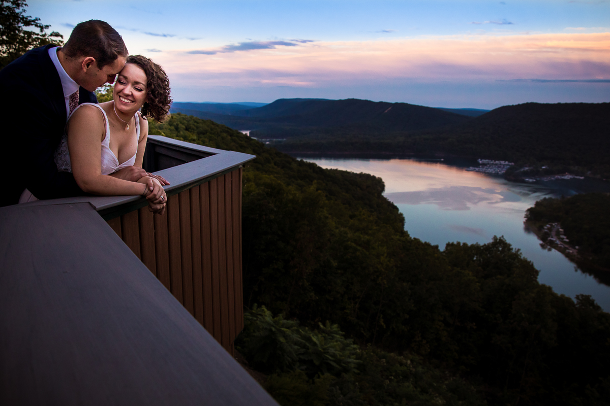 artistic colorful vibrant bride and groom standing on balcony smiling with raystown lake in background sunset