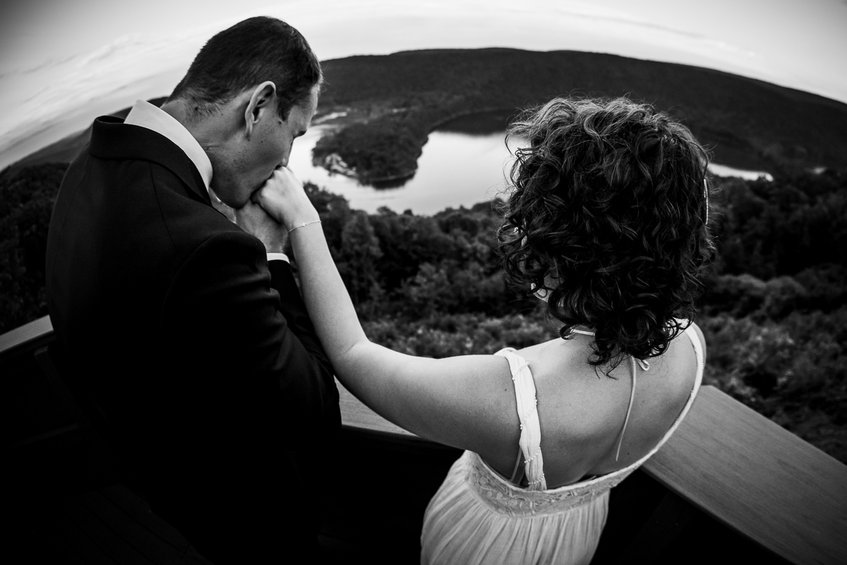 black and white photo of groom giving bride a kiss on the Hand standing on balcony with raystown lake in background