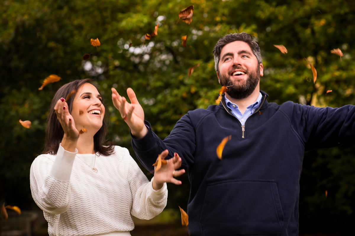 couple standing in gardens throwing up fall leaves in air
