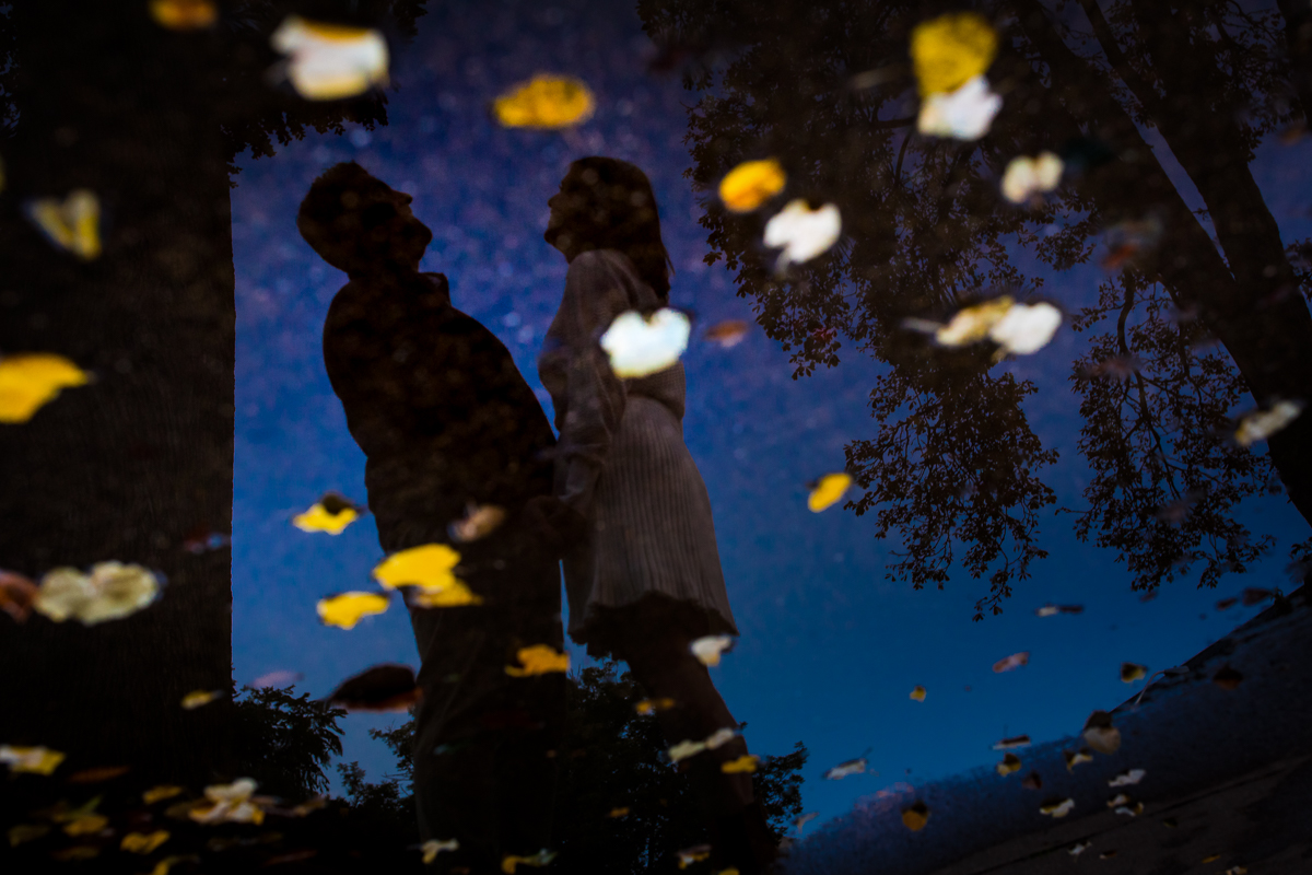 creative artistic engagement photographer couple reflected into puddle of water scattered with fall leaves