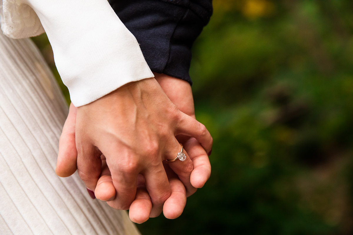 close up of couple holding hands with oval engagement ring