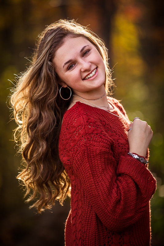 girl wearing red sweater with wavy brown hair smiling at camera