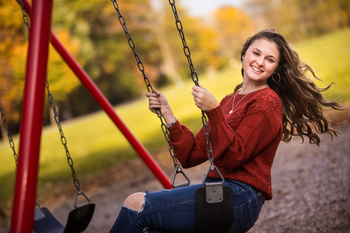 girl wearing red sweater swinging at park during senior portrait session 