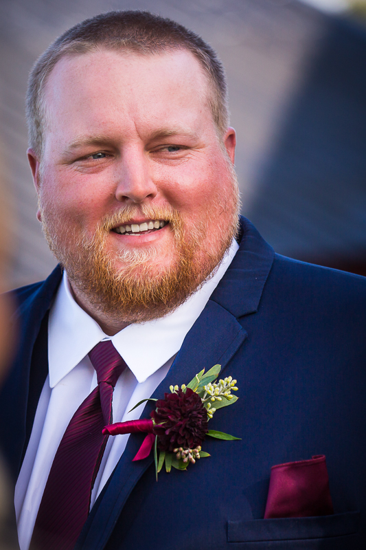 groom smiling with navy tux and maroon tie and flower