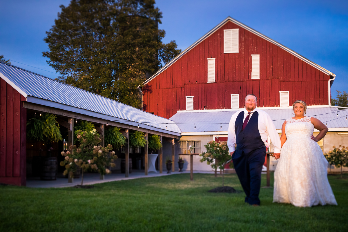 bride and groom walking outside heritage restored farm barn smiling holding hands 