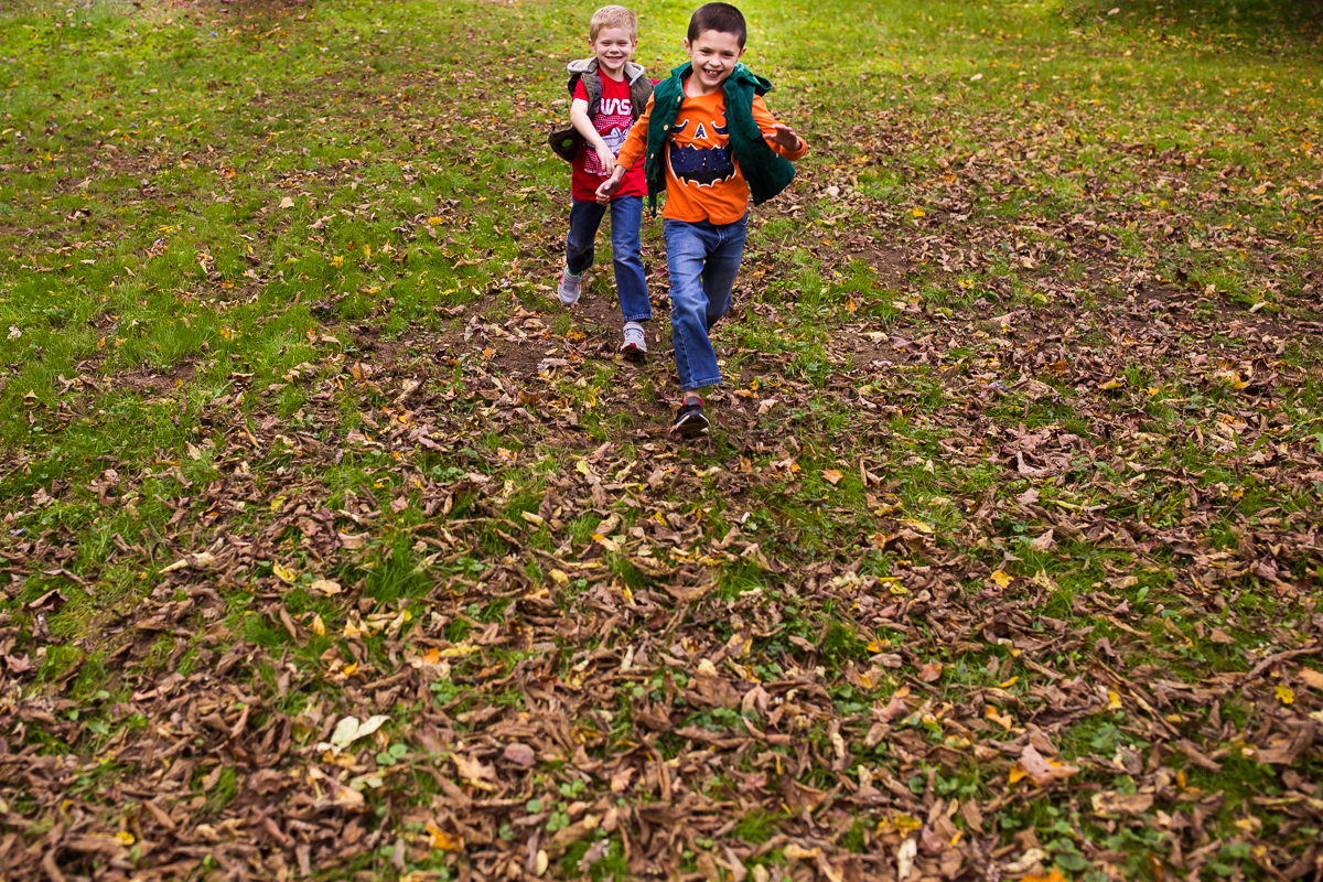 family lifestyle session two boys running through grass and leaves with vests and pumpkin shirt on 