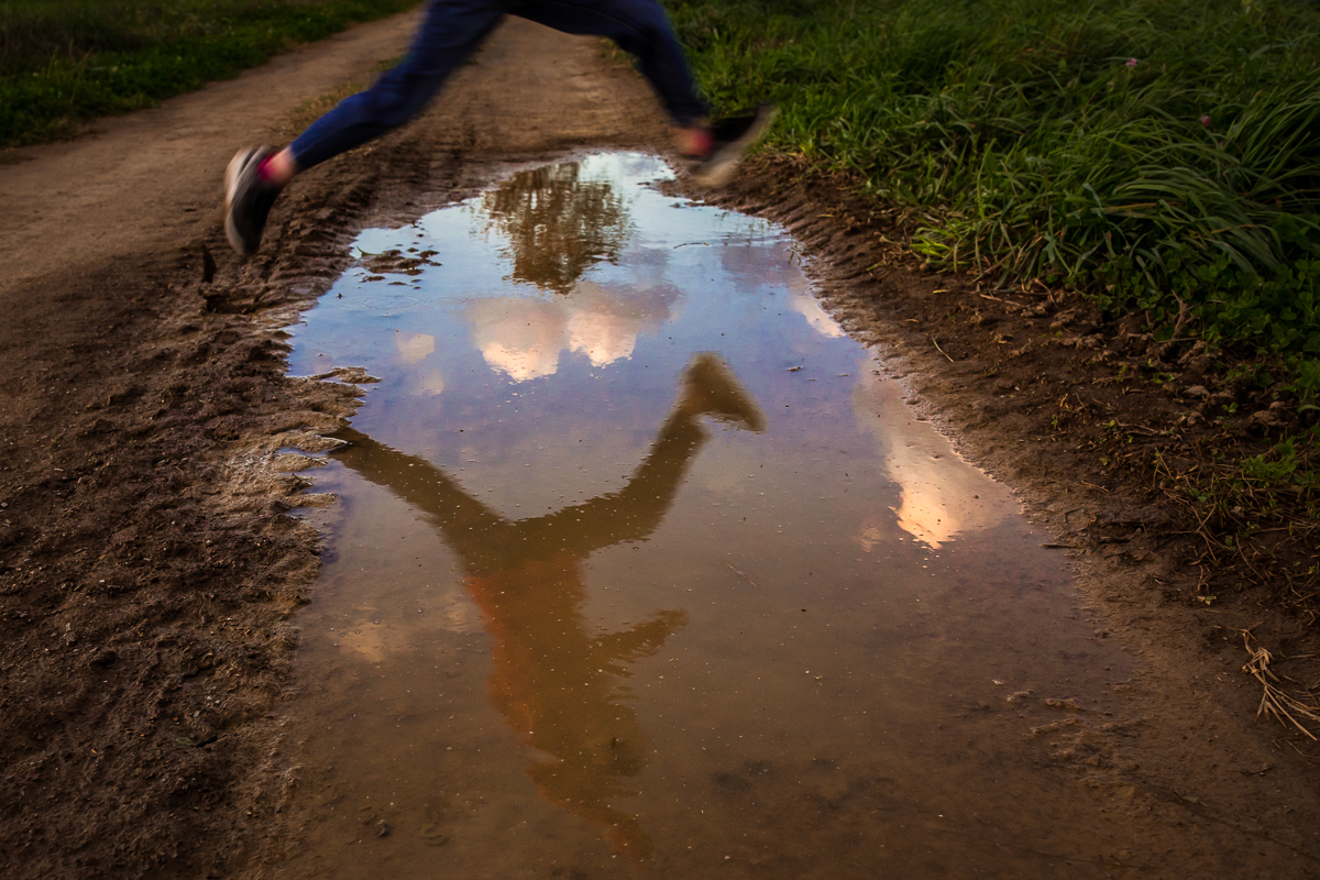 creative artistic family lifestyle session boy jumping over puddle reflection of sky 