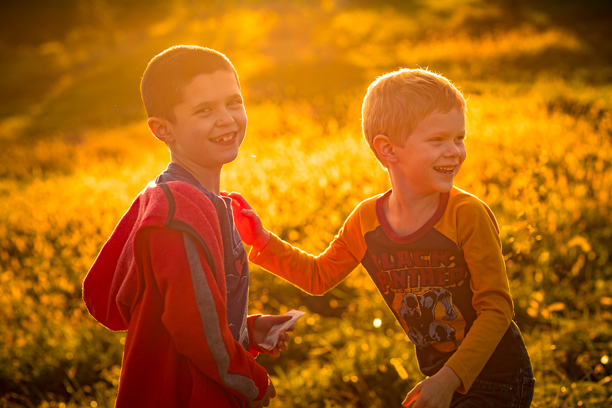 two boys smiling and laughing at camera golden hour light surrounding them