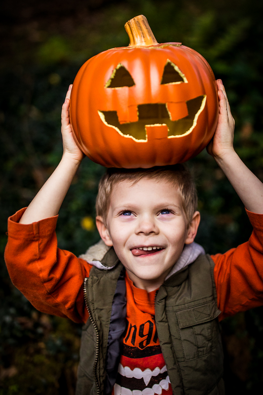 boy making silly face holding carved pumpkin on top of head