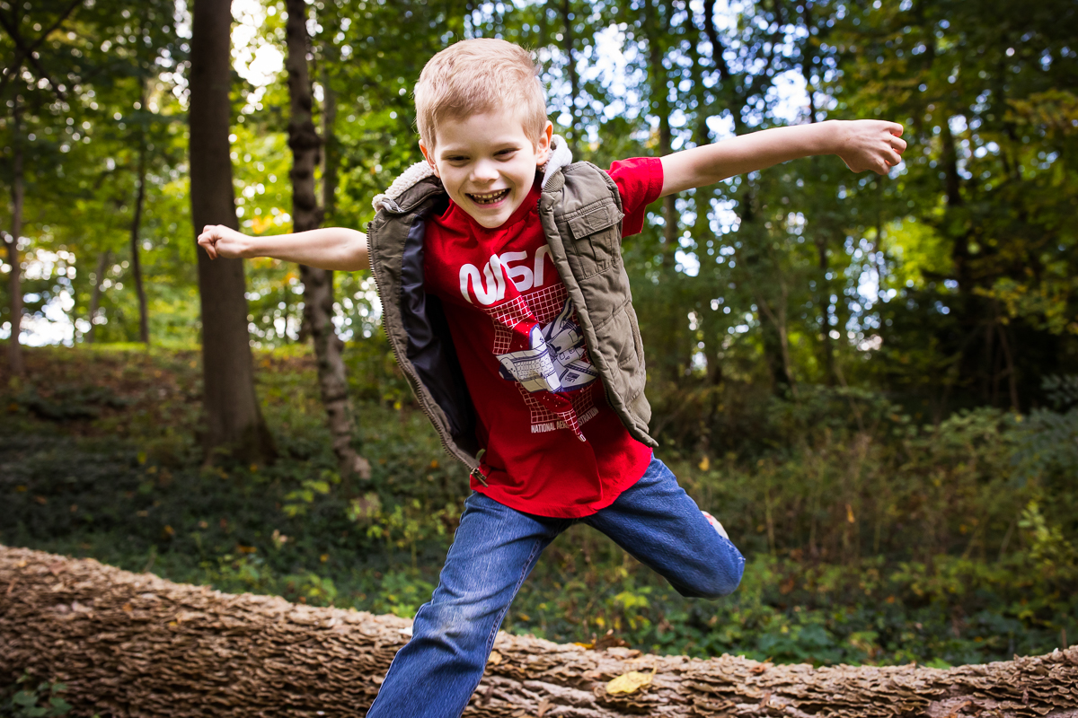 boy running and smiling and jumping over log in woods central pa family lifestyle session