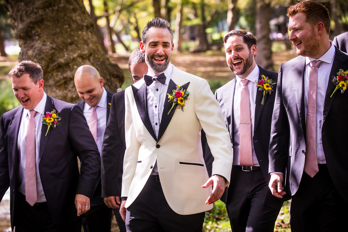 groom surrounded by groomsmen laughing and walking at illicks park