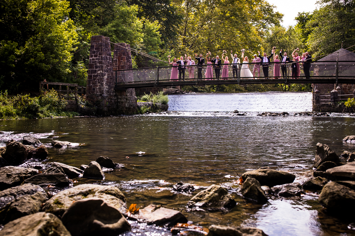 creative Lehigh Valley wedding party photographer standing on bridge waving over creek 