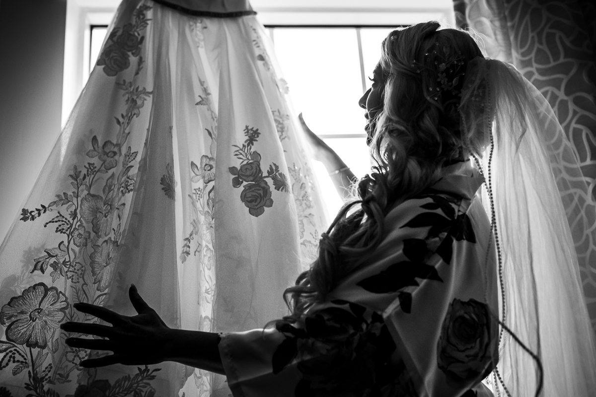 black and white photo of bride admiring lace wedding dress details during getting ready 