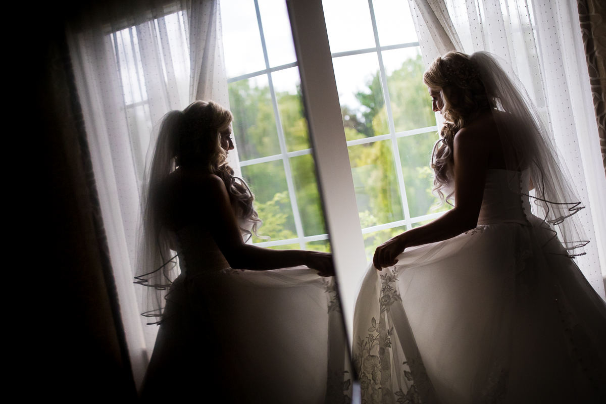 bride looking out window holding wedding dress artistic reflection in mirror creative wedding photographer pa