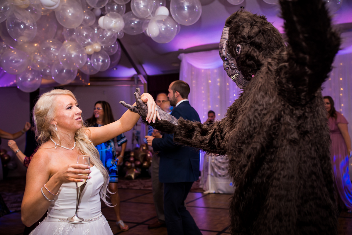bride dancing with person in gorilla costume spinning on dance floor with balloons in background