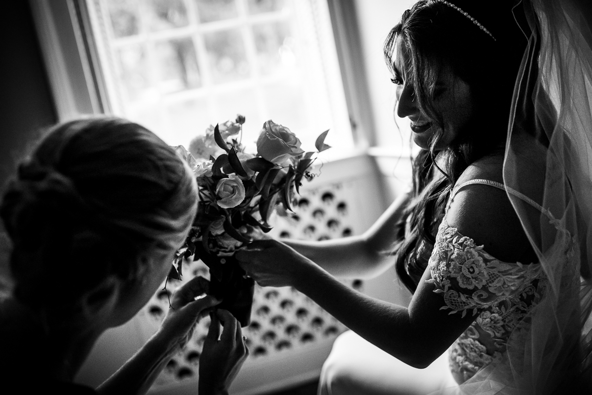 black and white photo of bridesmaid helping bride pin ribbon to bouquet 